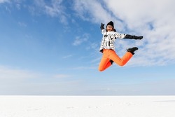 Young adult beautiful sporty happy attractive caucasian smiling hiker woman enjoy jumping high frozen lake surface panorama horizon background. Winter travel freedom outdoors adventure trip concept