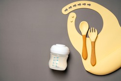 Children's tableware silicone bib, drinking bowl with milk and spoon, fork. Serving baby. Place for text.