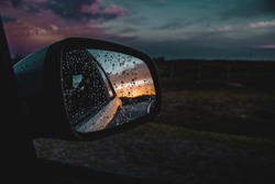 Car wing mirror view of an intense sunset during a rainy drive