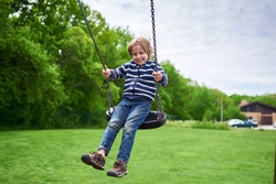 Outdoors portrait of cute preschool laughing boy swinging on a swing at the playground.
