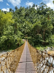 Swinging suspension bridge above river in tropical forest - Negros Oriental, Philippines	