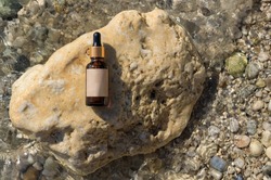 Bottle serum, cosmetic in clear, transparent water on stone, flat lay, top view, copy space. Blank label, mockup. Natural background, stones and water on the beach
