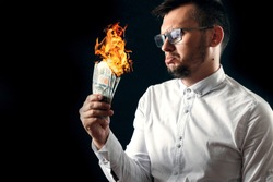 A man holds burning money in his hands, burning US dollars. The concept of inflation, a decrease in the purchase of foreign currency, and devolution.