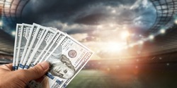 Close-up of a man's hand holding US dollars against the background of the stadium. The concept of sports betting, making a profit from betting, gambling. American football