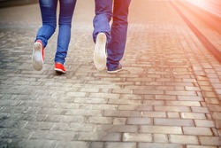 Legs close-up of a loving couple running along a sidewalk tile, romance, love, blue jeans, sneakers. Concept idyll.