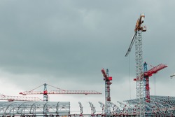 Construction site. Big industrial tower cranes with unfinished high raised buildings and blue sky in background. Scaffold. Modern civil engineering. Contemporary urban landscape.