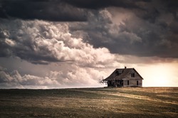Old wooden farmhouse in the countryside at sunset with storm  clouds in the sky. There is a short grass meadow around the house.