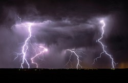 Lightning streak from a thunderstorm cloud at night in a rural setting. There are multiple lightning strikes coming from the thunderstorm.
