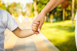 Cropped close up of a boy and grandmother holding hands. CLose up of hands of a child and parent on the walk at the local park in summer family love bonding children parenting family weekend leisure