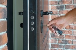The man inserts the key into the lock to close the armored door of the house.                               