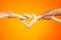 Image of a heart in the form of a rope knot. Male and female hands hold on to a thick rope. Knot tightening. The concept of strong love and inextricable relationship.                                