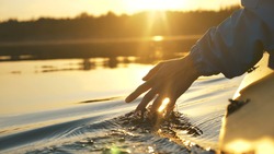man puts fingers down in lake kayaking against backdrop of golden sunset, unity harmony nature