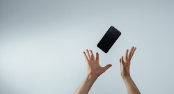 A view of the hand that tosses or catches a mobile phone. The smartphone is falling, hands are trying to catch it. The concept of communication, attempts to connect and talk.
