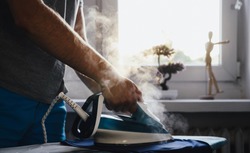 Man is ironing clothes. The concept of caring for the home, helping men in household chores. The man uses an iron to iron the child's clothes.