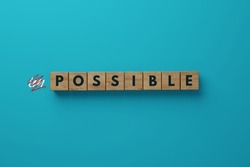 Wooden blocks on a blue background with the word possible and crossed out IM. Eliminating the impossible against the possible.