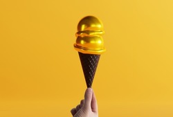 Hand holds ice cream in a black waffle on the ground and yellow background. The concept of eating ice cream, cooling down. Modern ice cream with a black waffle.