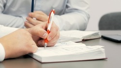 Employee in the conference room makes notes in his notebook while discussing a business plan. Close-up of the employee's hand.