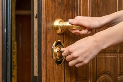 Woman's hands open a brown front door with a gold handle with a key close up
