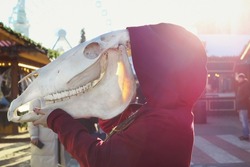 Close up animal skull concept photo. Lady holding horse cranium. Side view photography with city street on background. High quality picture for wallpaper, travel blog, magazine, article