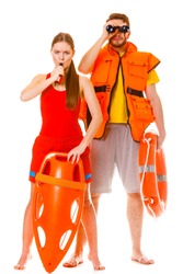 Lifeguards with rescue tube ring buoy lifebuoy and life vest jacket looking through binoculars. Man and woman supervising swimming pool whistling. Accident prevention.