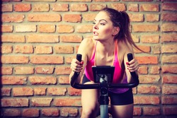 Active woman wearing sport bra working out,  using exercise bike at the gym. Sporty girl training in fitness center. Slim body weight loss concept. 