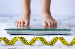 Weight control concept with centimeter in focus and blurred kid's feet on digital scale in the background. Child measuring weight, healthy growing. 