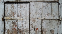 Old gray barn door with hand wrought iron hinges. Old cracked paint on wooden background texture. From old age, almost all the coating peeled off.