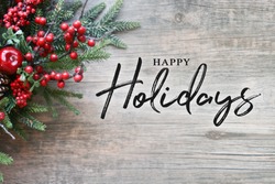 Happy Holidays Text with Christmas Evergreen Branches and Berries in Corner Over Rustic Wooden Background