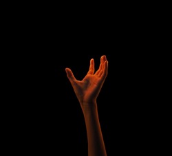 Isolated hand reaching to grab some source of light in the black background.