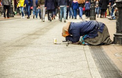 The old homeless woman kneels in the street as passersby pass by and pray for money.