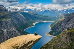 Amazing nature view with Trolltunga and a girl sitting  on it. Location: Scandinavian Mountains, Norway, Odda. Artistic picture. Beauty world. The feeling of complete freedom.