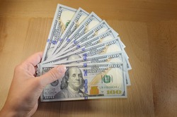 Hand holding one hundred dollar bills on wooden background