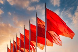 Red flags, the symbol of the Chinese communist party blow in the wind in the center of Beijing Tiananmen Square. Sunset sky in background with no recognisable buildings. 