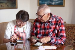 Senior couple counting money, filling checks and control finance sitting at the table in the living room