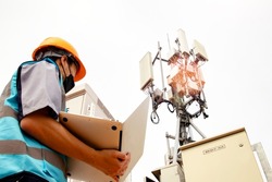 Masked man electronics asian worker  skilled control IT system, control cabinet, station telecommunication tower uses laptop to inspect 5G network technology telecommunications circuit board system.
