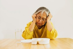 Asian elderly woman sits and looks upset eats boring, bland nutrient poor boxes has no appetite does not like to eat : Unhealthy foods and foods high in fat and high in cholesterol : Soft focus