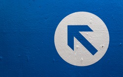 Directional arrow on a blue wall pointing upwards and left.