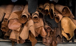 Different pieces of leather in a rolls. The pieces of the colored leathers. Rolls of natural brown red leather. Raw materials for manufacture of bags, shoes, clothing and accessories.