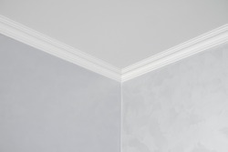 White ceiling with a white plinth in a room with gray painted walls. Decoration of the corner between the ceiling and the wall in the room. Ceiling molding in the interior. Detail of corner.