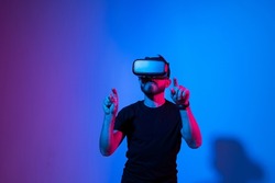 Future technology, gaming, entertainment and people concept - happy young man with virtual reality headset or 3d glasses playing video game in metaverse.