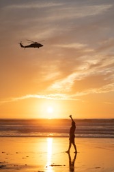 A young girl waves to a helicopter passing overhead on Mission Beach, San Diego, California