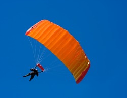 Parachuter descending with a orange parachute against blue sky