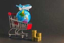 Toy plane on  background of  globe and  grocery cart with coins. Concept of airfare, air travel, air insurance.