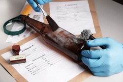Forensic fingerprint analysis, criminalist collects latent fingerprints using fingerprint powder on a glass bottle close-up