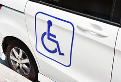 A handicap sign on the side of the white car. Handicapped people in car.