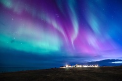 colorful northern lights in a iceland landscape with cottage mountain and sea