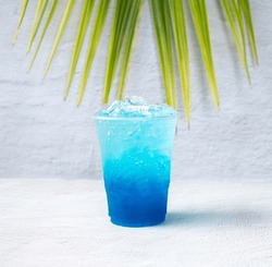 Blue Hawaiian drink in a plastic glass and coconut leaves.