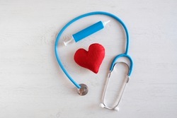 Medical stethoscope, blue syringe toy, red soft toy heart. Concept cardiology, therapeutic procedures. Light wooden background.