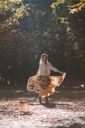 Smiling woman in cozy wear dancing in autumn park in raise of sunlight.