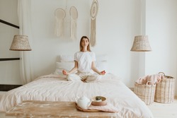 Beautiful young woman practicing meditation on the bed.
